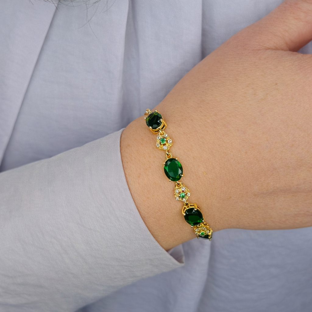 Gouden damesarmband met groene stenen en verfijnde details, gedragen om de pols