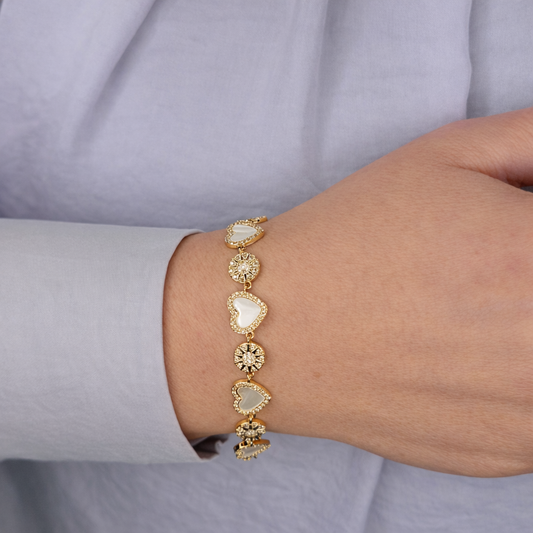 Gouden damesarmband met hartvormige parelmoer elementen en fonkelende zirkonia details, gedragen om de pols.