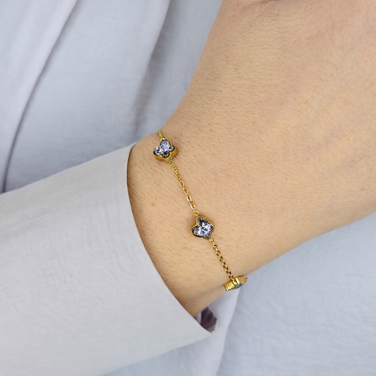 Gouden dames armband met fijne schakelketting en vier bloemvormige kristallen, elegant gedragen om de pols