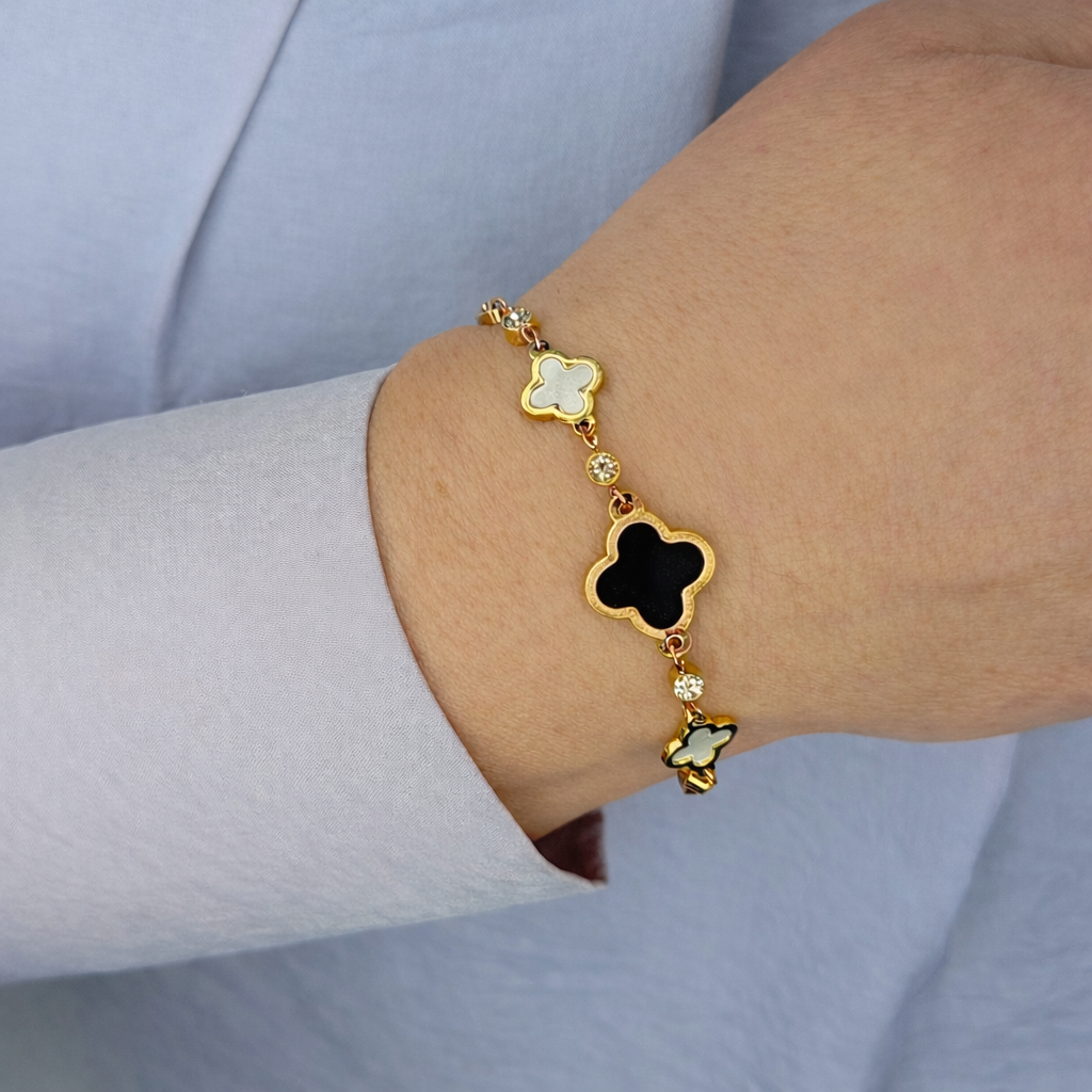 Gouden klaver armband met zwarte en witte details gedragen om de pols, elegant en luxe uitstraling