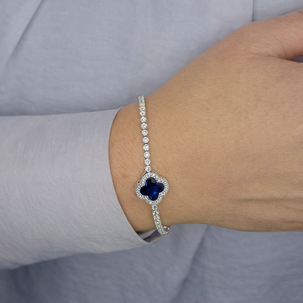 Zilverkleurige armband met fonkelende zirkonia stenen en centrale transparante steen, gedragen om de pols tegen een lichte achtergrond.