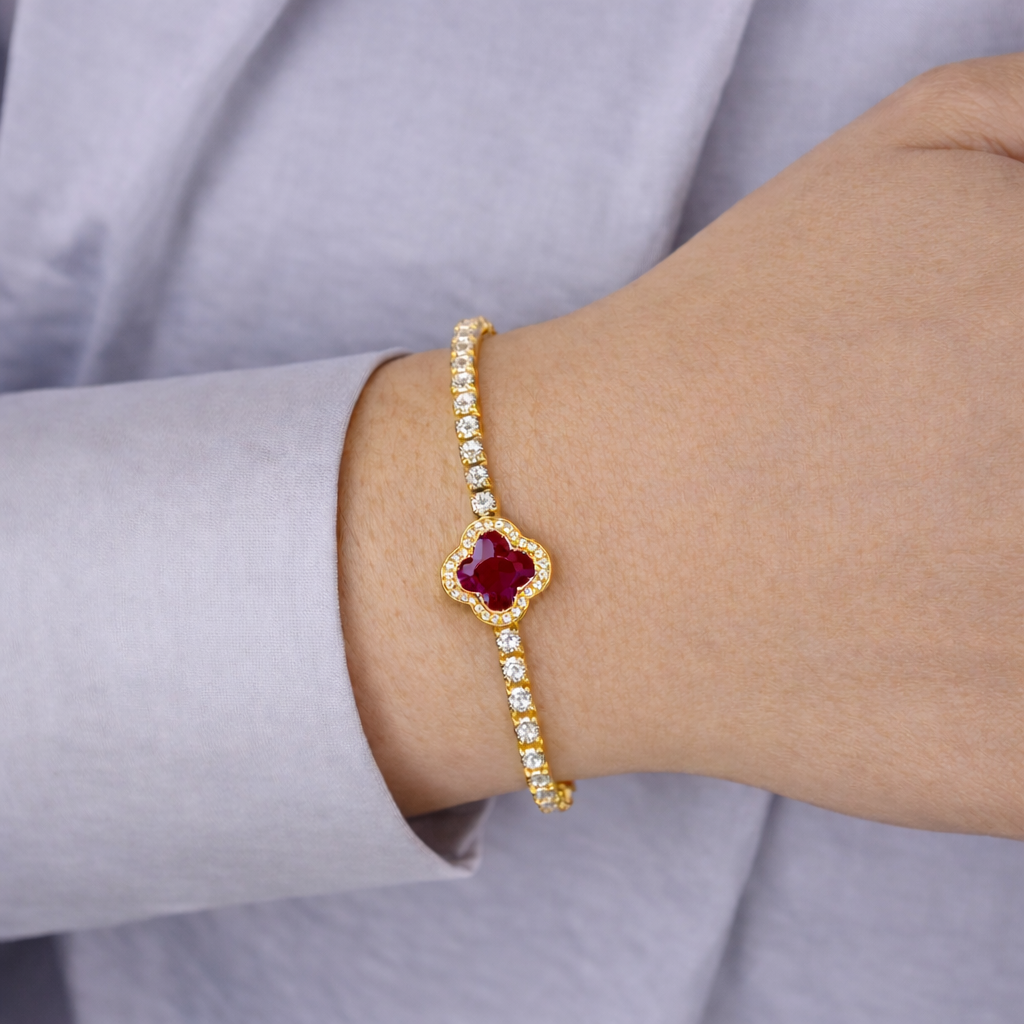 Gouden armband met rode klaversteen en fonkelende zirkonia, gedragen om de pols