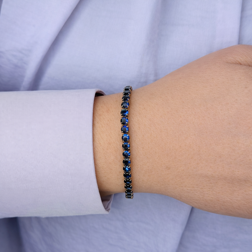 goudkleurige armband met donkerblauwe kristallen, gedragen om de pols, gefotografeerd van dichtbij tegen een lichte achtergrond voor een luxe productpresentatie.