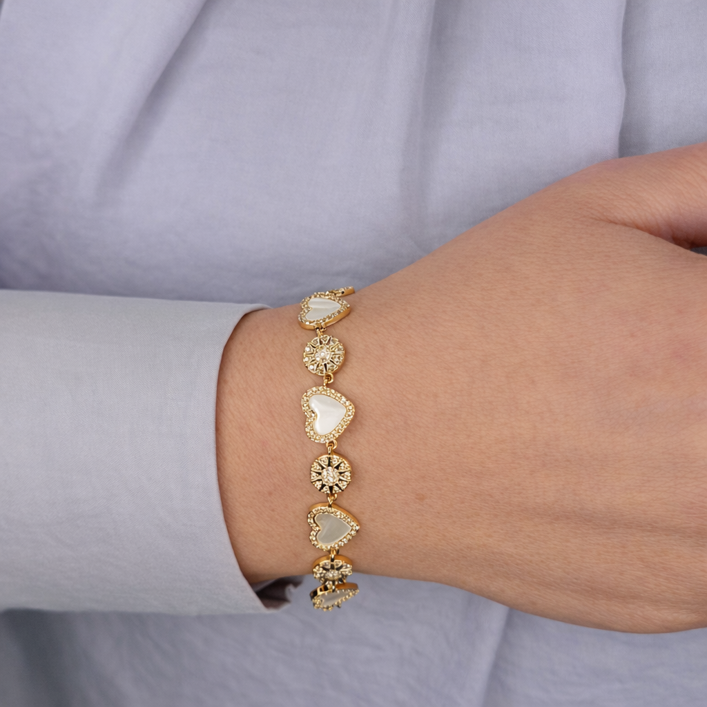 Gouden damesarmband met hartvormige parelmoer elementen en fonkelende zirkonia details, gedragen om de pols.