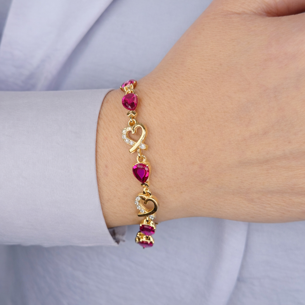 Gouden damesarmband met paarse hartvormige stenen en hartdetails met fonkelende kristallen, gedragen om de pols op een lichte achtergrond.