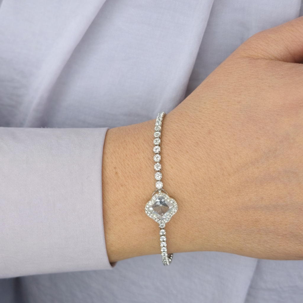 Zilverkleurige armband met fonkelende zirkonia stenen en centrale transparante steen, gedragen om de pols tegen een lichte achtergrond.