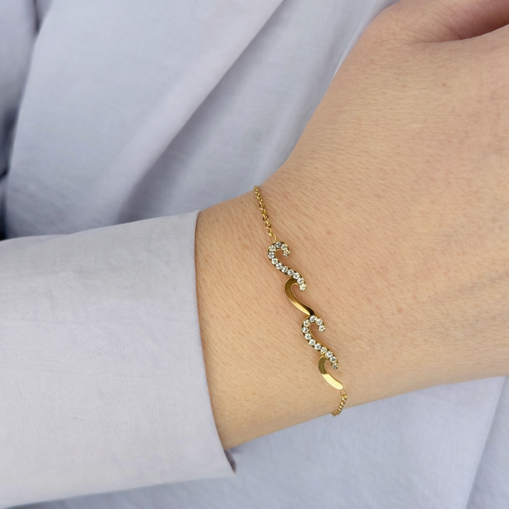 goud damesarmband met golvend S-design en fonkelende zirkonia stenen, elegant gedragen om de pols.