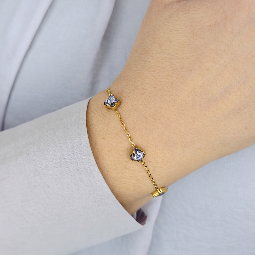 Gouden dames armband met fijne schakelketting en vier bloemvormige kristallen, elegant gedragen om de pols