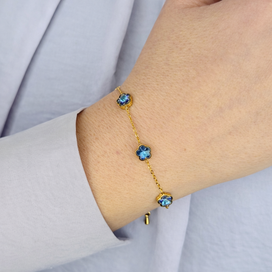 Gouden damesarmband met drie blauwe klaverstenen, gedragen om de pols, verfijnd en elegant design.