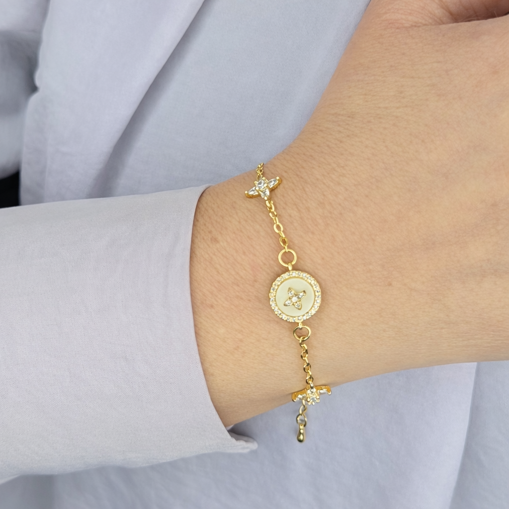 Gouden damesarmband met fijne schakelketting, ronde bedel met parelmoerlook en zirkonia steentjes, gedragen om de pols tegen een lichte achtergrond.