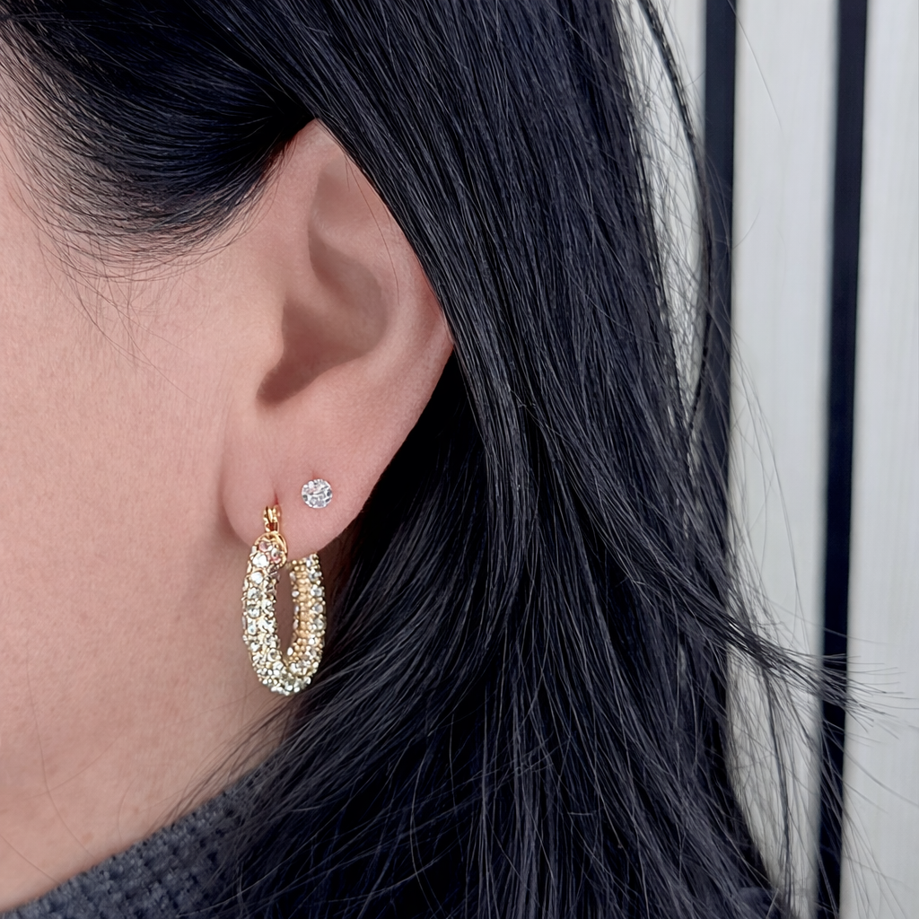 gouden oorringen met zirkonia gedragen door vrouw, close-up van oor met glanzende zilveren oorbel op productfoto.