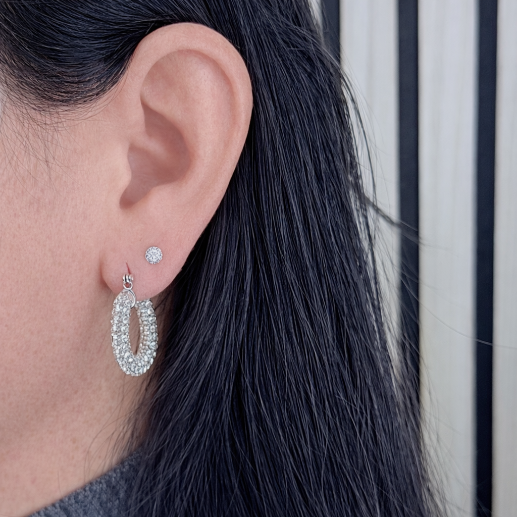 Zilveren oorringen met zirkonia gedragen door vrouw, close-up van oor met glanzende zilveren oorbel op productfoto.