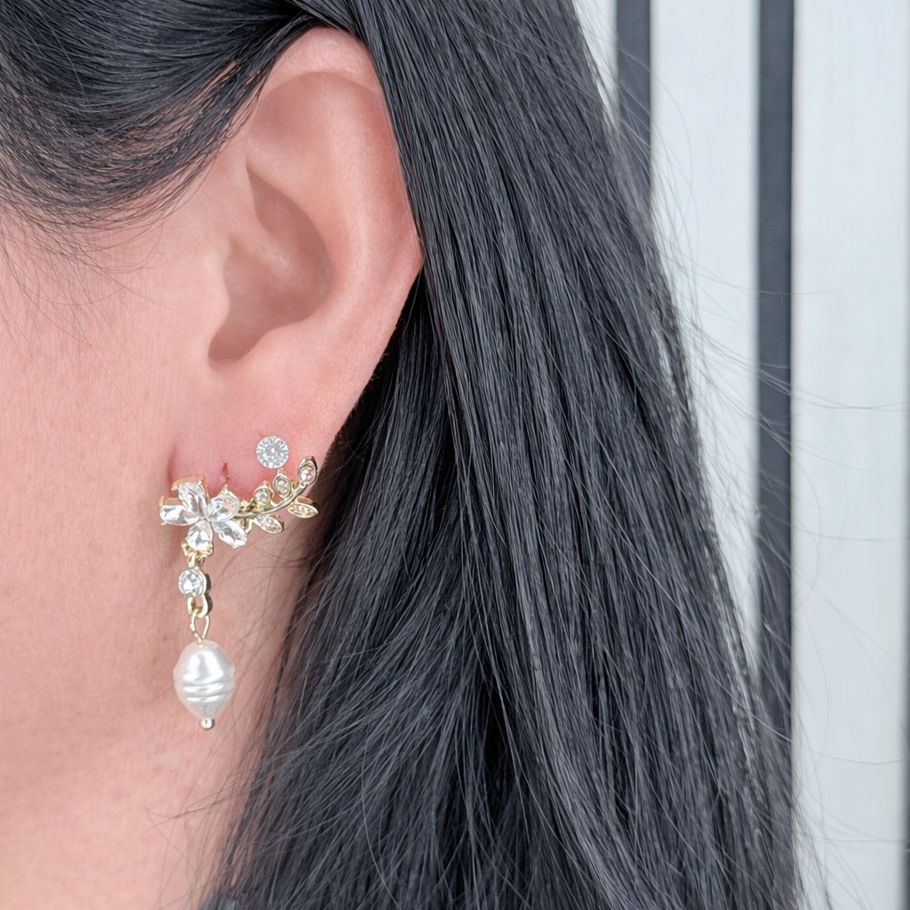 Gouden bloemoorbel met zirkonia en hangende parel, close-up productfoto gedragen aan het oor met gladde huid zonder zichtbare oorgaatjes.