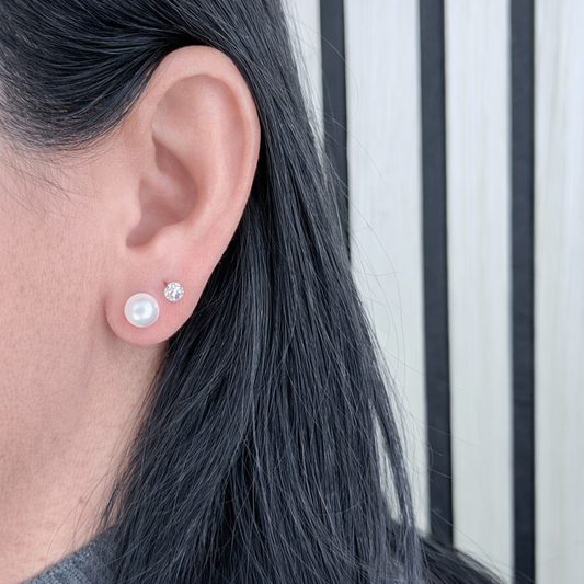 Zilveren parel oorbel met zirkonia steker, close-up gedragen in het oor, scherpe productfoto op lichte achtergrond.