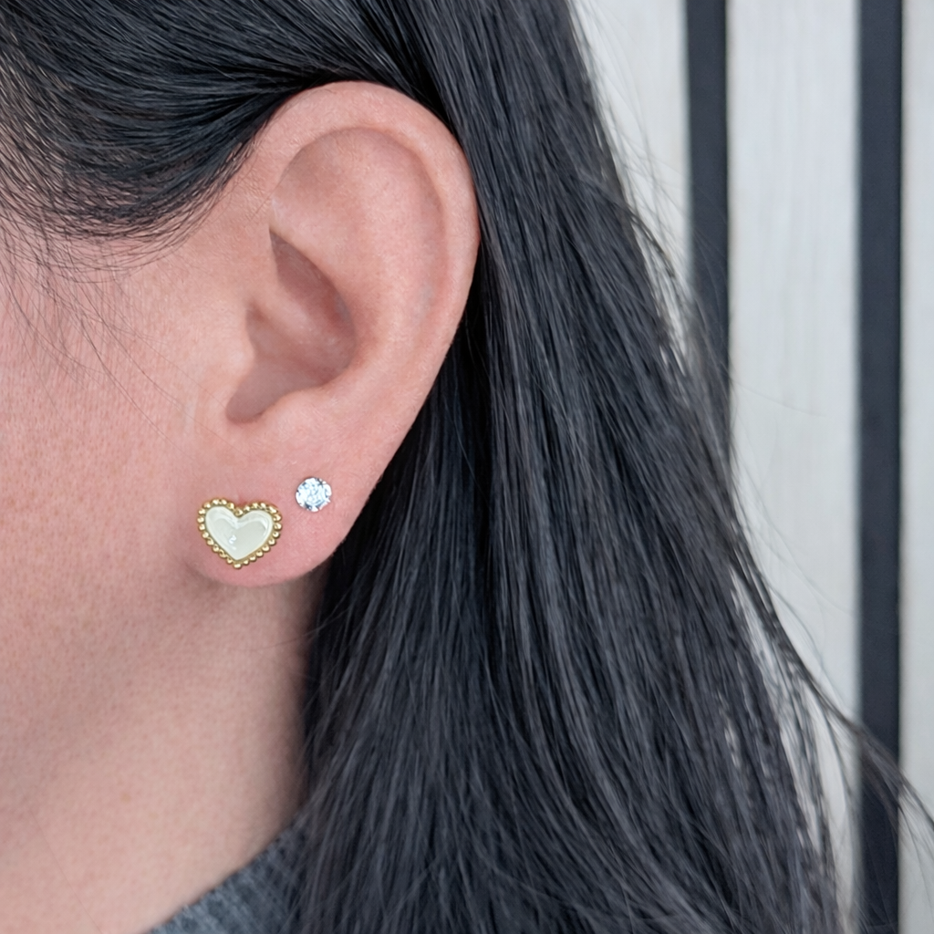 witte hartvormige oorbel met gouden rand en zirkonia steentje, gedragen in het oor – scherp productdetail op lichte achtergrond.