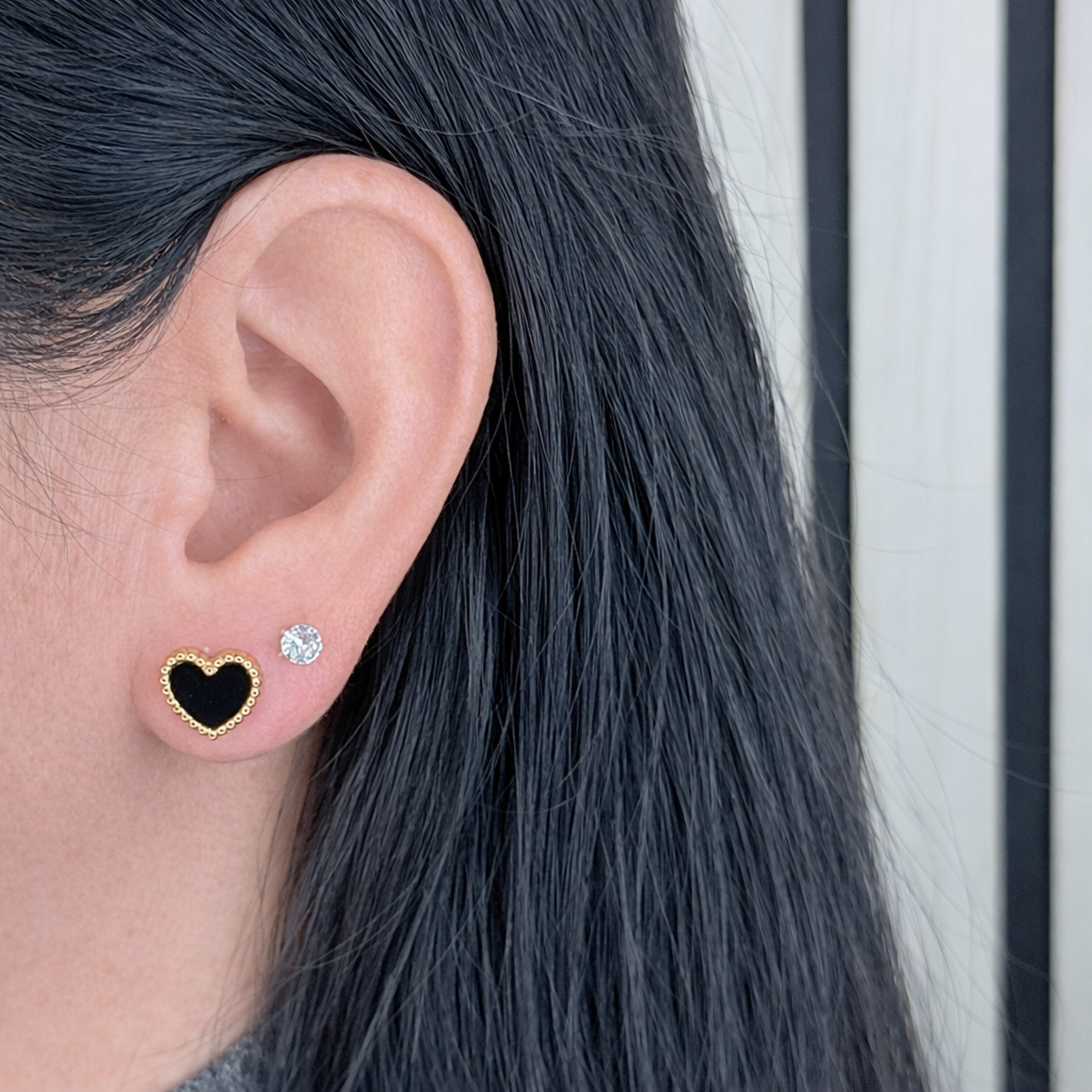 Zwarte hartvormige oorbel met gouden rand en zirkonia steentje, gedragen in het oor – scherp productdetail op lichte achtergrond.