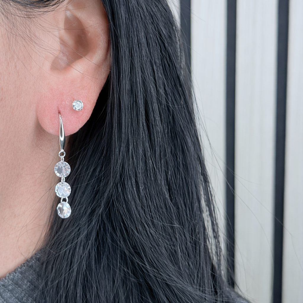 Zilveren hangende oorbel met drie fonkelende zirkonia stenen, gedragen in het oor, scherp en gedetailleerd gefotografeerd.