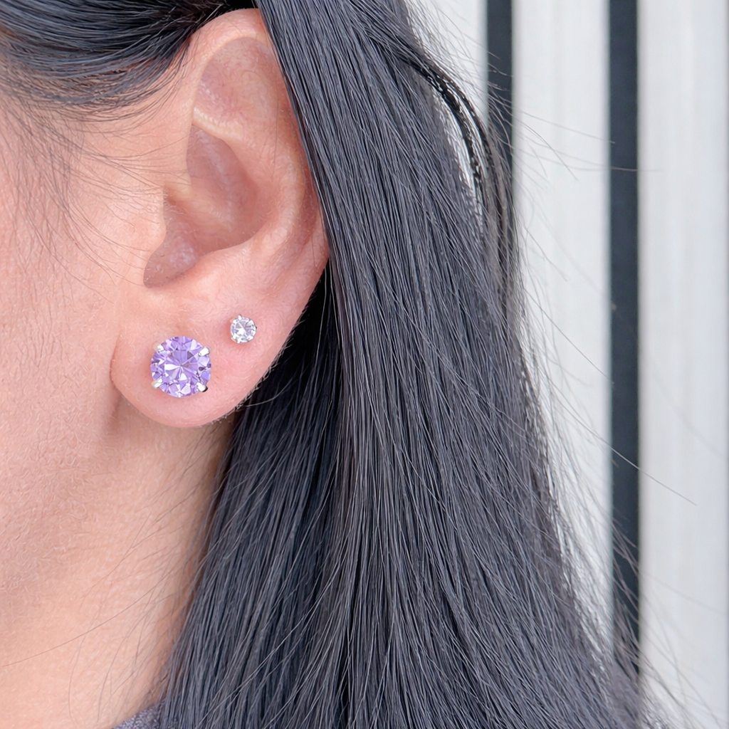 paarse zirconia oorstekers van zilver, ronde solitaire studs gedragen in het oor met natuurlijke lichtinval.