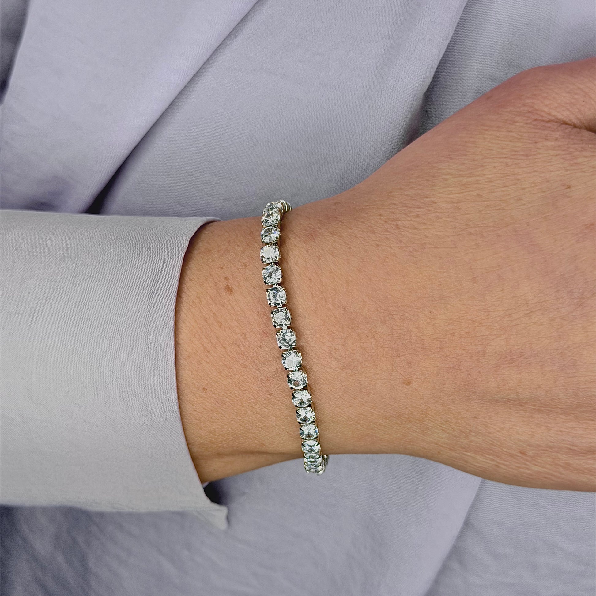 Zilveren tennisarmband met heldere kristallen, gedragen om de pols, gefotografeerd tegen een lichte achtergrond met verfijnde glans en details zichtbaar.